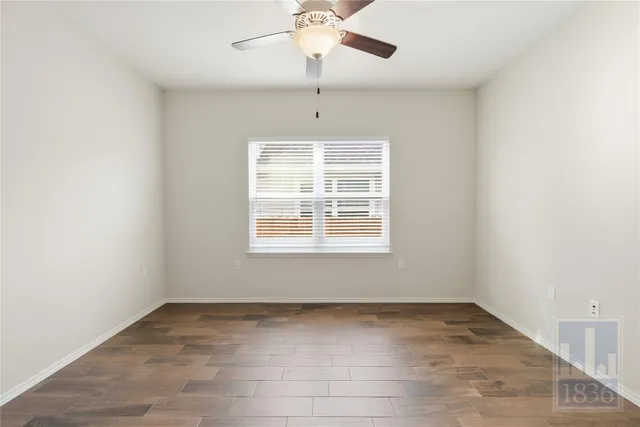 an empty room with chandelier fan and windows