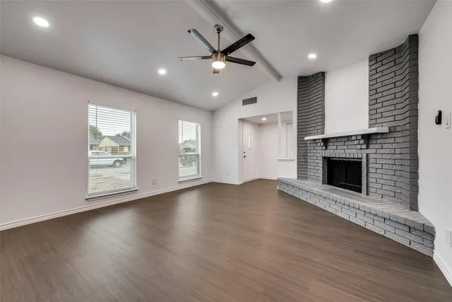 an empty room with windows a fireplace a ceiling fan and wooden floor