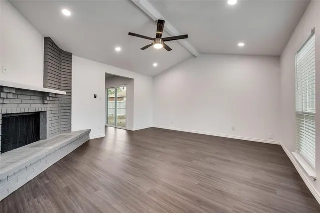 an empty room with wooden floor fireplace and windows