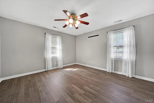 an empty room with wooden floor chandelier fan and windows