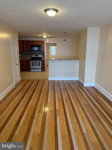 a view of kitchen and empty room with wooden floor