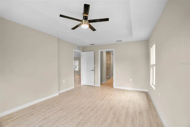an empty room with wooden floor a ceiling fan and windows