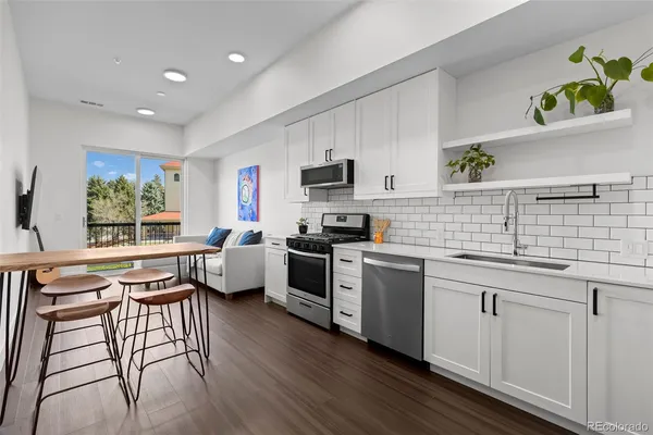 a kitchen with stainless steel appliances granite countertop a stove top oven a sink a dining table and chairs with wooden floor