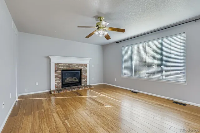 a view of an empty room with wooden floor fireplace and a window