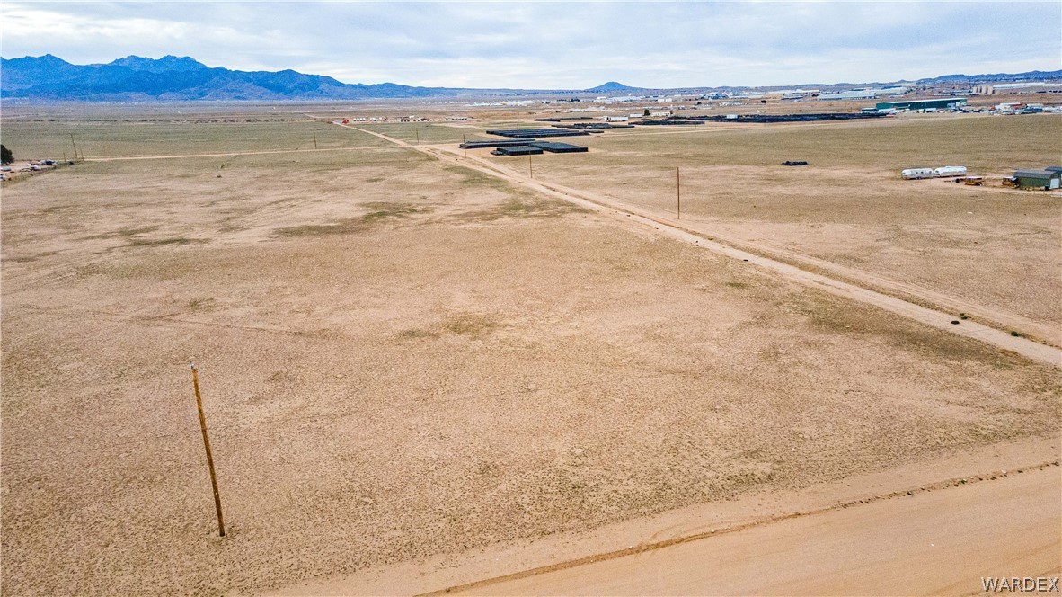 0 East Parker Road, Unit 119 Kingman, AZ 86401 - Photo 8 of 16 Expansive undeveloped land featuring a dirt road, minimal vegetation, distant mountains, and distant industrial structures