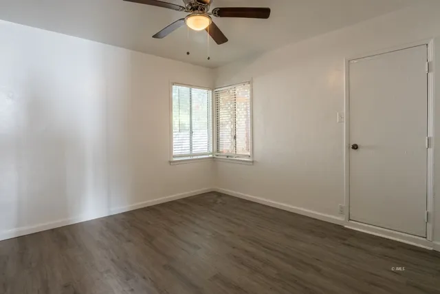 an empty room with wooden floor fan and windows