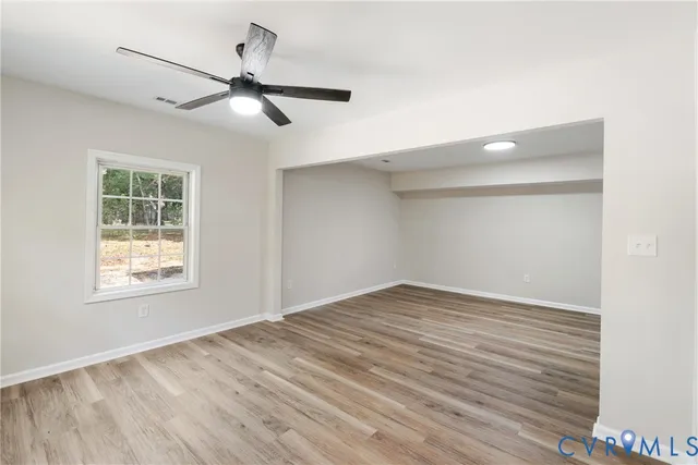 an empty room with wooden floor chandelier fan and windows