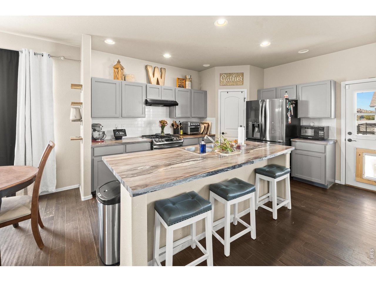 8847 16th St Road Greeley, CO 80634 - Photo 12 of 38 a kitchen with stainless steel appliances kitchen island granite countertop a dining table chairs and refrigerator