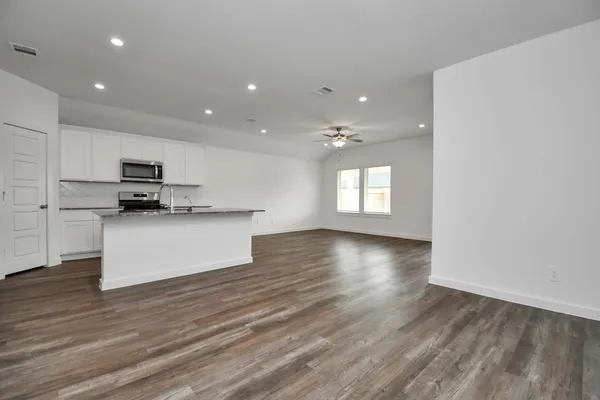 an empty room with wooden floor fan and windows