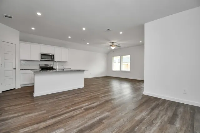 an empty room with wooden floor fan and windows