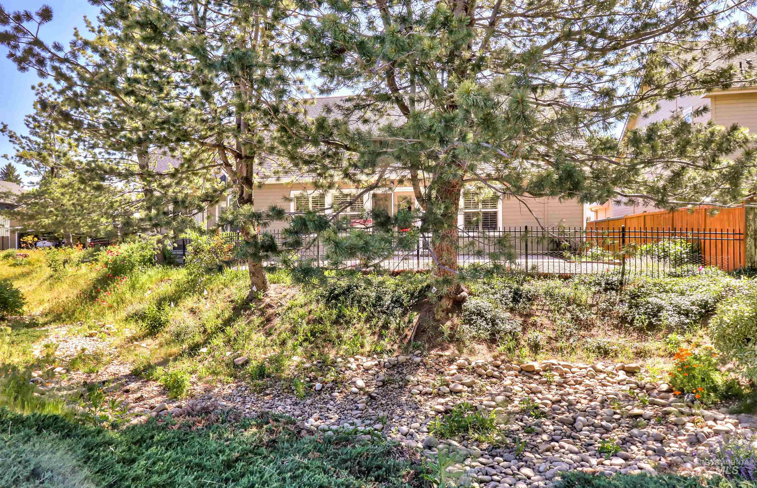 892 South Capitola Way Boise, ID 83712 - Photo 29 of 34 Landscaped backyard with a black wrought iron fence, wood privacy fence, and mature pine trees