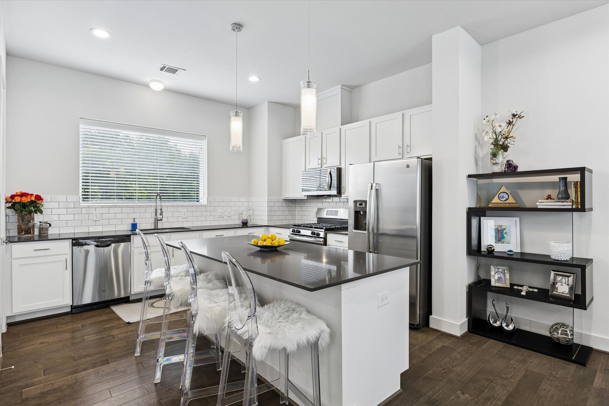 1310 Hussion Street Houston, TX 77003 - Photo 12 of 34 The modern kitchen features sleek white cabinetry, stainless steel appliances, and a large island with seating. The space is brightened by pendant lighting and a window, while a dark wood floor adds warmth.
