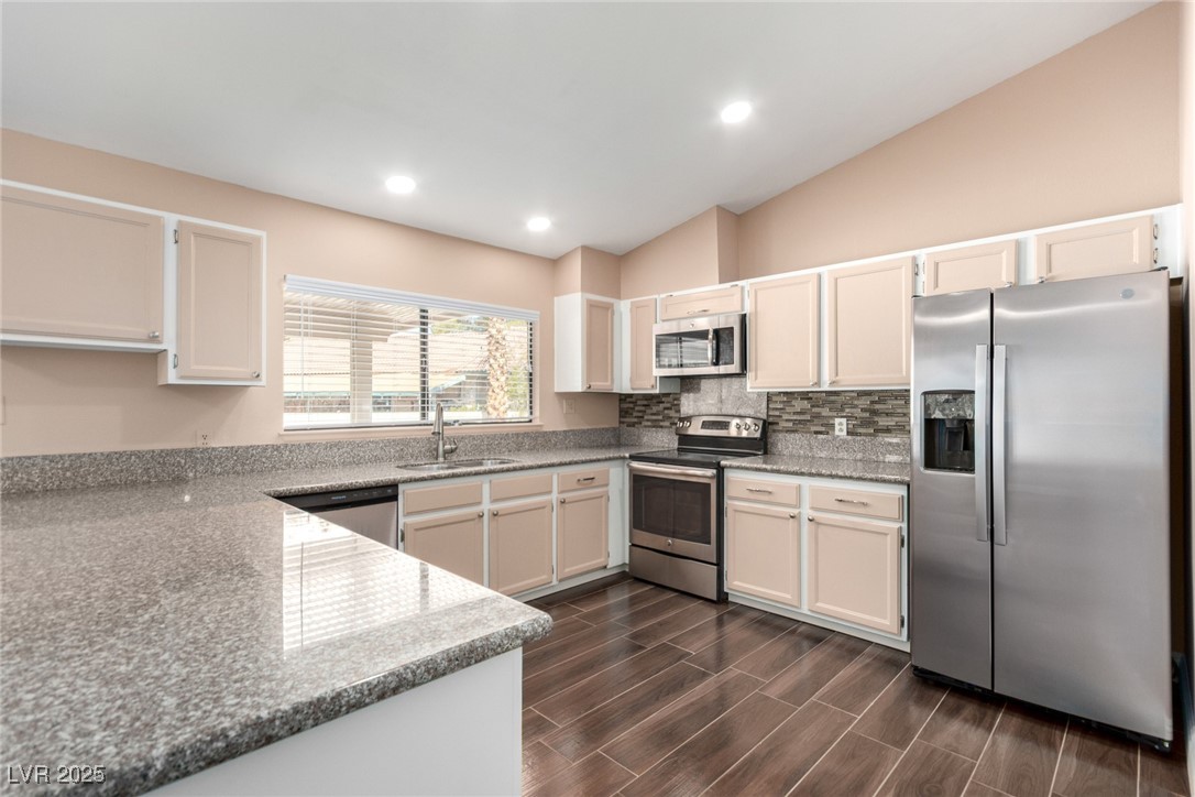 6465 West Plumcrest Road Las Vegas, NV 89108 - Photo 12 of 34 Kitchen featuring appliances with stainless steel finishes, light stone counters, recessed lighting, lofted ceiling, and tasteful backsplash