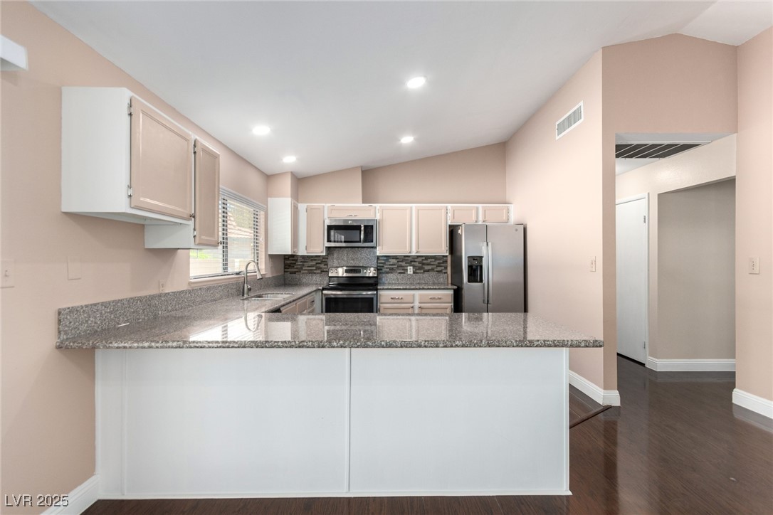 6465 West Plumcrest Road Las Vegas, NV 89108 - Photo 13 of 34 Kitchen with lofted ceiling, appliances with stainless steel finishes, dark stone countertops, a peninsula, and dark wood-type flooring