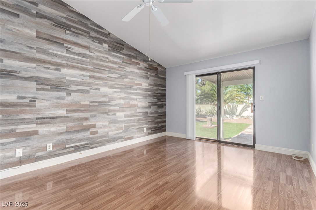 6465 West Plumcrest Road Las Vegas, NV 89108 - Photo 17 of 34 Empty room featuring light wood-type flooring, wooden walls, vaulted ceiling, an accent wall, and ceiling fan
