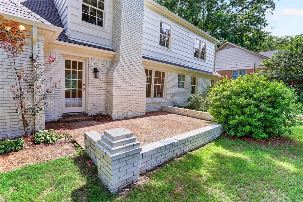 7674 Apple Valley Road Germantown, TN 38138 - Photo 14 of 15 White-painted brick exterior featuring a French door with multiple glass panes, an exterior wall lantern, a brick chimney, and an outdoor patio with a low brick retaining wall