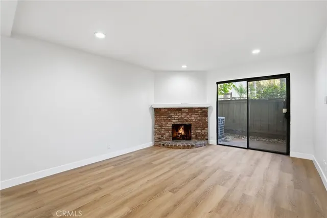 a view of an empty room with wooden floor fireplace and a window