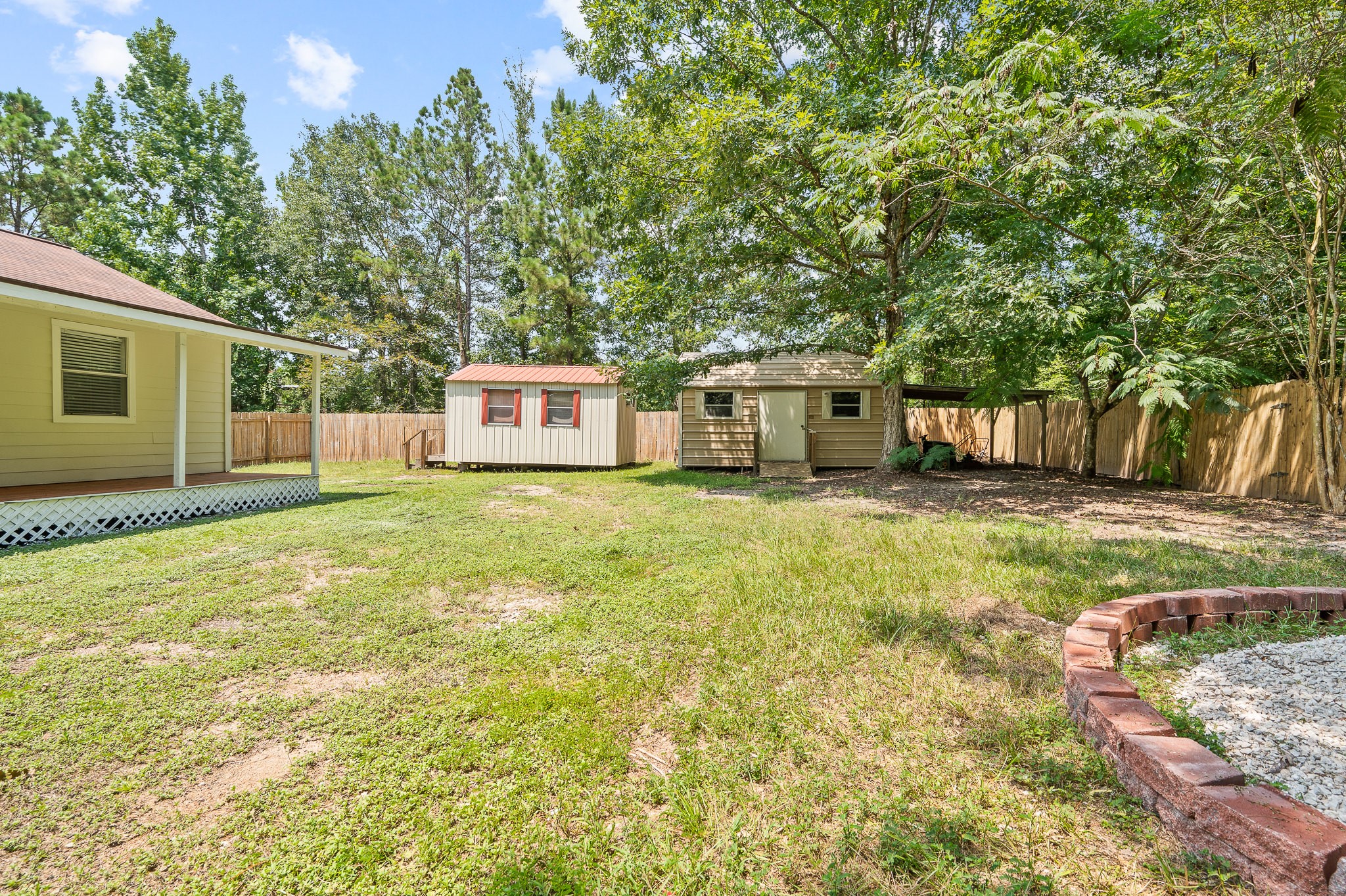 61 Hicks Loop West Cleveland, TX 77328 - Photo 30 of 38 Spacious backyard featuring two charming storage sheds, lush greenery, and a privacy fence, ideal for outdoor activities and storage solutions.