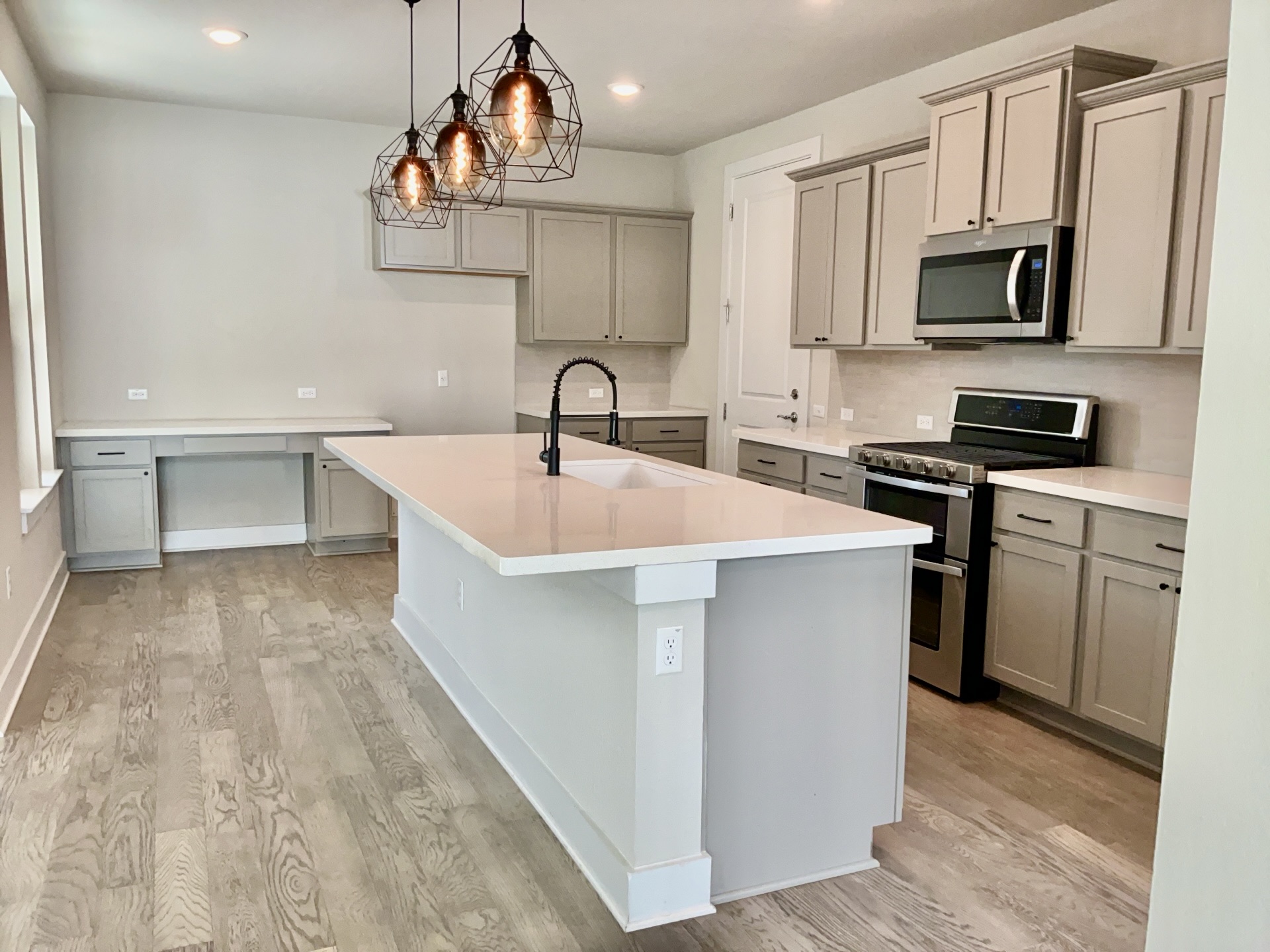 8315 Laughlin Lane Austin, TX 78744 - Photo 5 of 23 Kitchen featuring gray cabinetry, stainless steel appliances, pendant lighting, light wood finished floors, and a kitchen island with sink