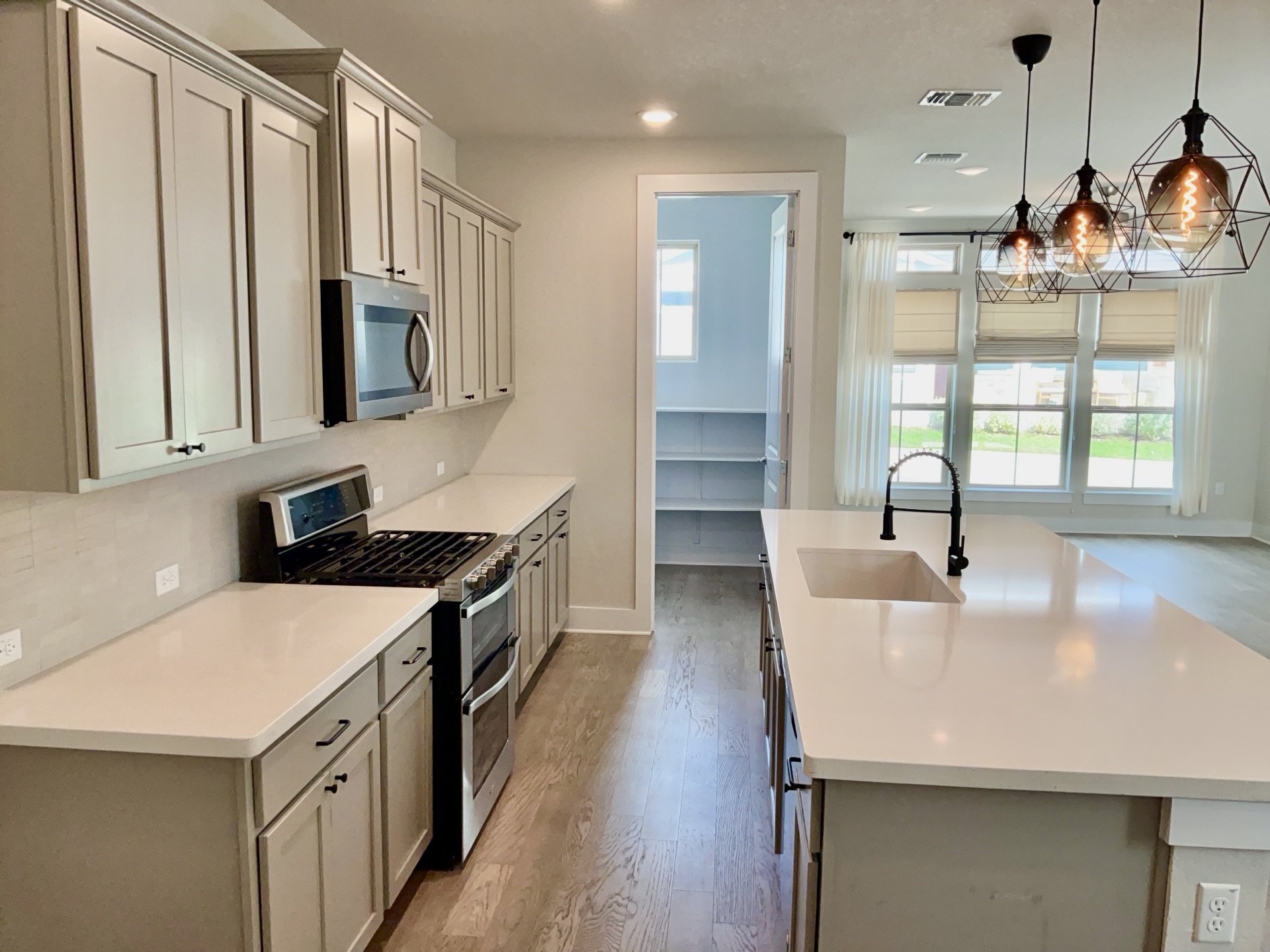 8315 Laughlin Lane Austin, TX 78744 - Photo 6 of 23 Kitchen with stainless steel appliances, a center island with sink, light wood-style flooring, hanging light fixtures, and light stone countertops