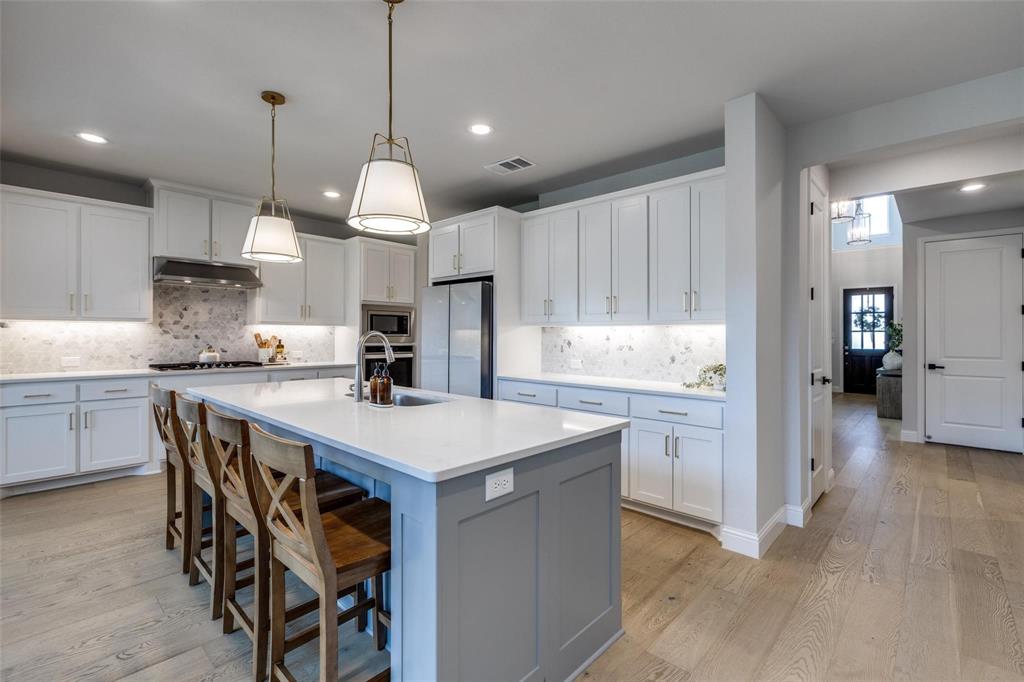 1000 Adair Road Prosper, TX 75078 - Photo 22 of 38 Oversized island has room for FOUR chairs and the expansive countertops give you room to spread out and get the chores done. In the back is a vented hood cooktop and notice that this entire main living area has NO carpeiing. They paid for beautiful wide plank wood flooring to create a beautiful place to spend time with your family and friends. Never Rented and the original owner is downsizing to another home so this immaculate home will NOT LAST! Call today...