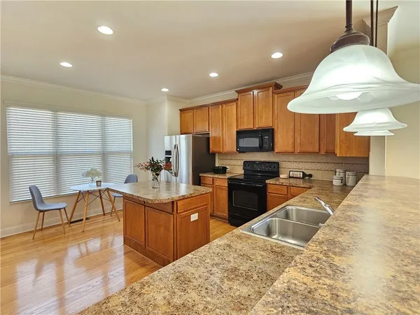 a kitchen with stainless steel appliances granite countertop a stove top oven a sink a dining table and chairs with wooden floor