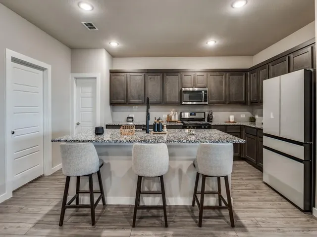 a kitchen with stainless steel appliances kitchen island granite countertop a refrigerator a stove a sink and white cabinets with wooden floor