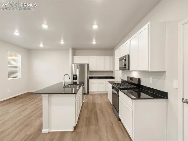 a kitchen with granite countertop a stove top oven a sink a refrigerator white cabinets and wooden floor
