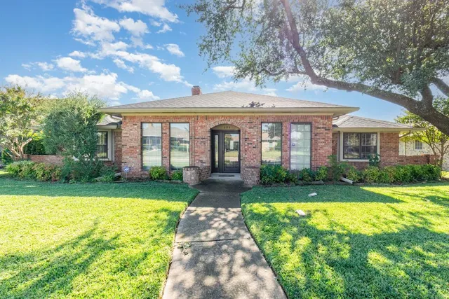 a view of a brick house with a big yard and large trees