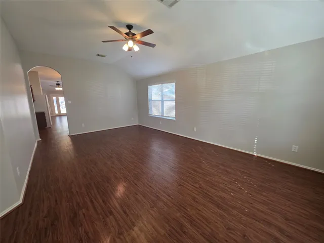 a view of an empty room with wooden floor and a ceiling fan