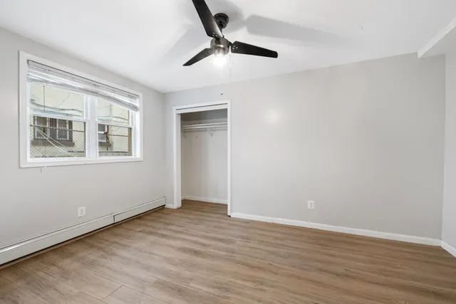 a view of an empty room with wooden floor and a ceiling fan