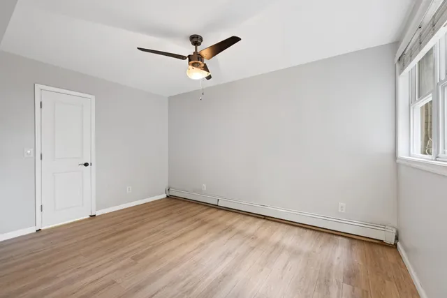 an empty room with wooden floor fan and windows