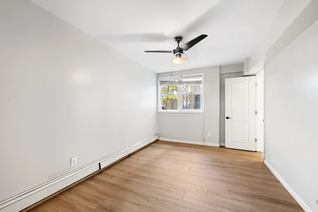 an empty room with wooden floor ceiling fan and windows