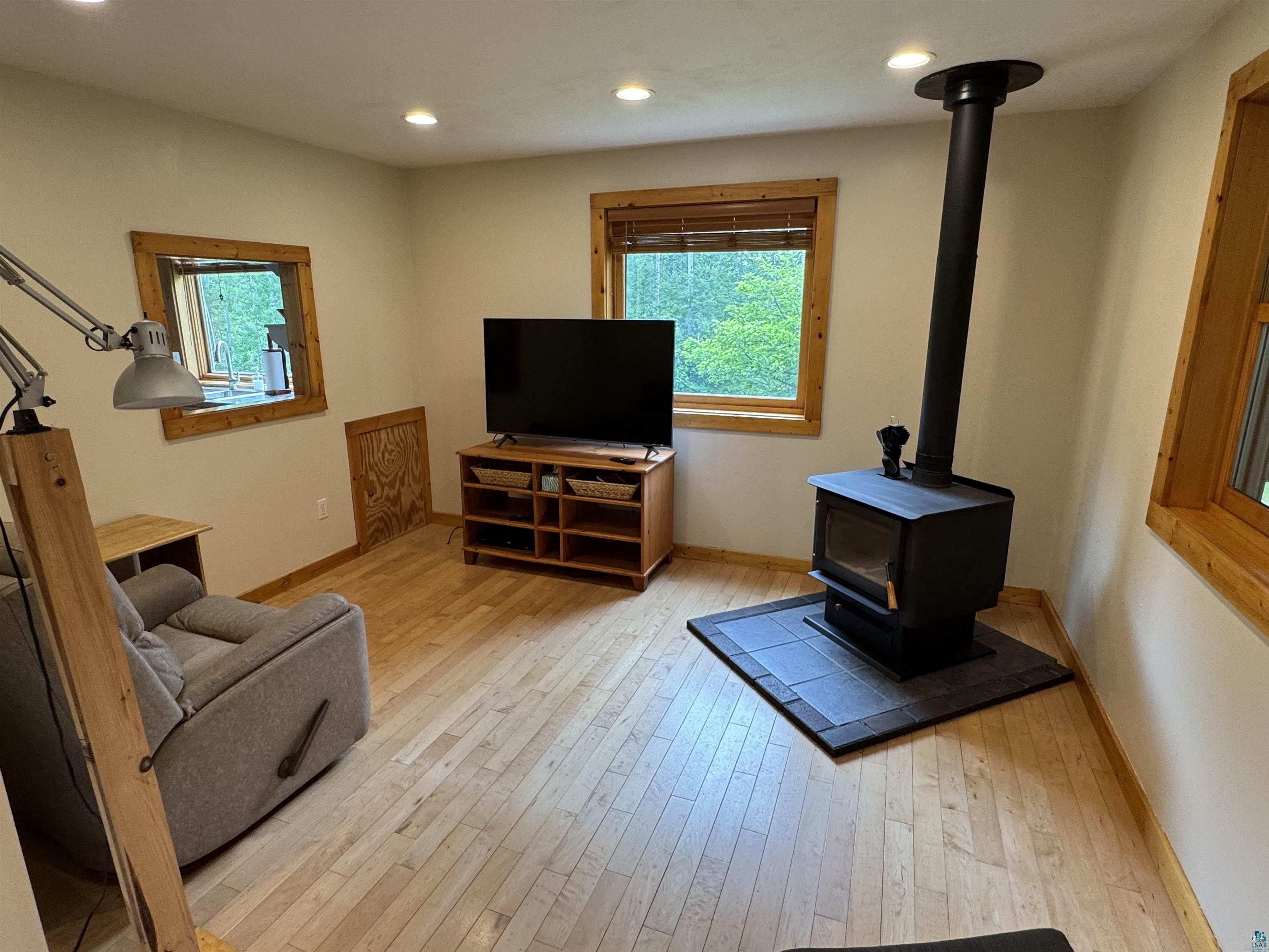 1745 Becks Road Maple, WI 54854 - Photo 6 of 46 Living area featuring a black wood-burning stove with a tile hearth, light wood-finish flooring, recessed ceiling lighting, and natural wood window trim