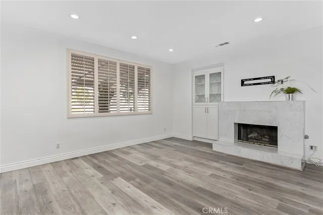 a view of an empty room with wooden floor fireplace and a window