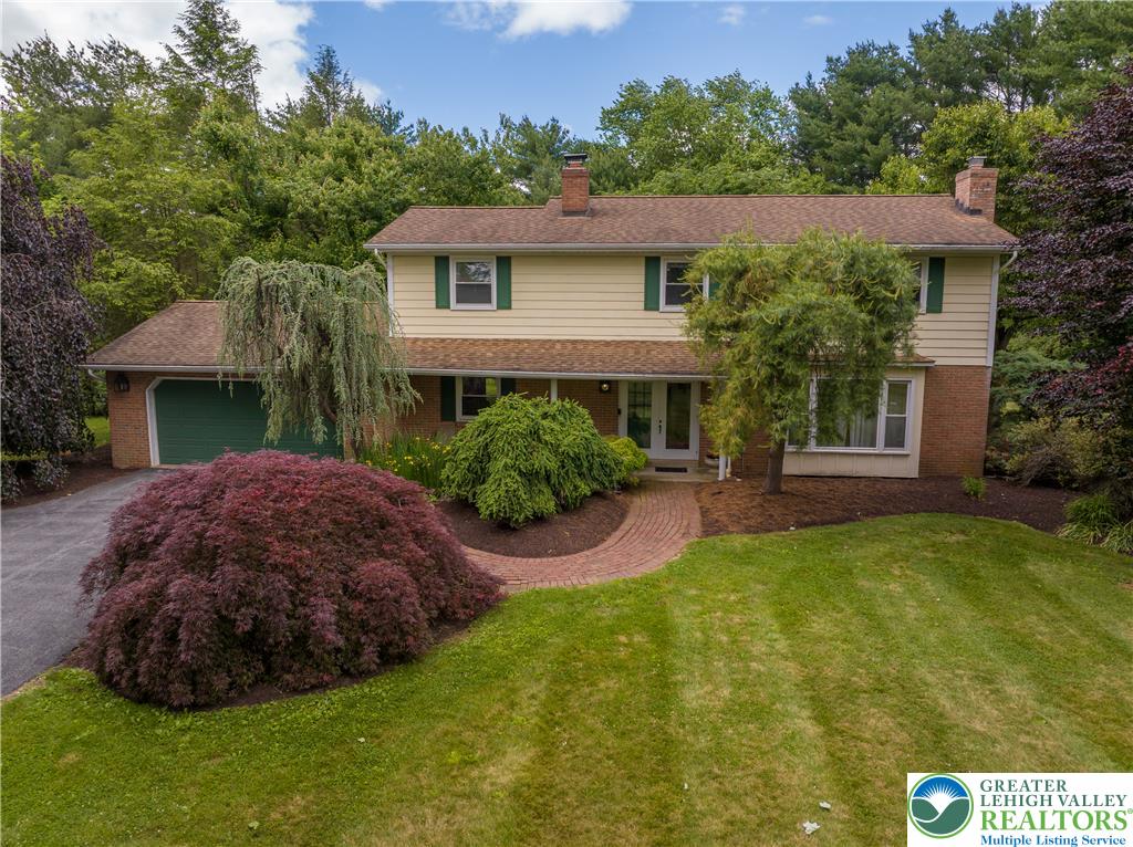 A classic facade featuring brick and siding, complemented by a winding brick path and lush, established landscaping.