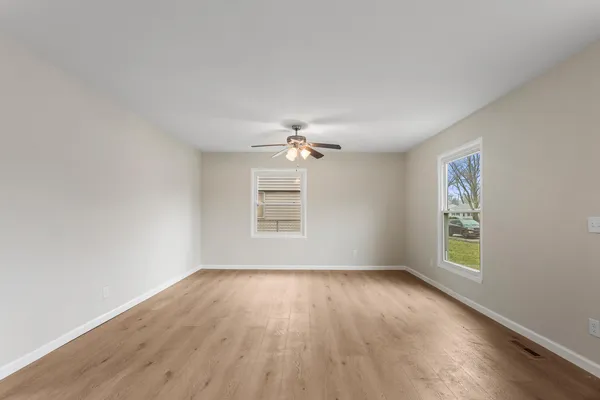 an empty room with wooden floor ceiling fan and windows