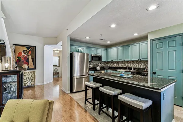 a kitchen with stainless steel appliances kitchen island granite countertop a stove a refrigerator a sink a dining table and chairs with wooden floor