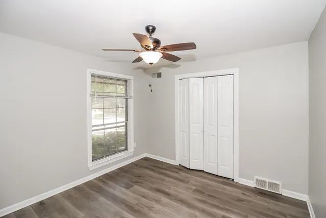 an empty room with wooden floor fan and windows