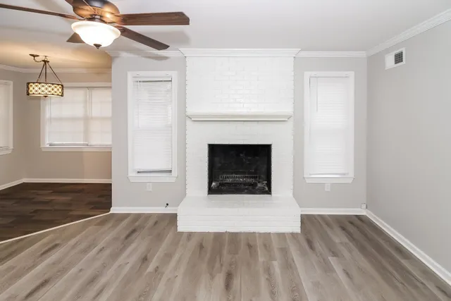 an empty room with wooden floor fireplace and windows