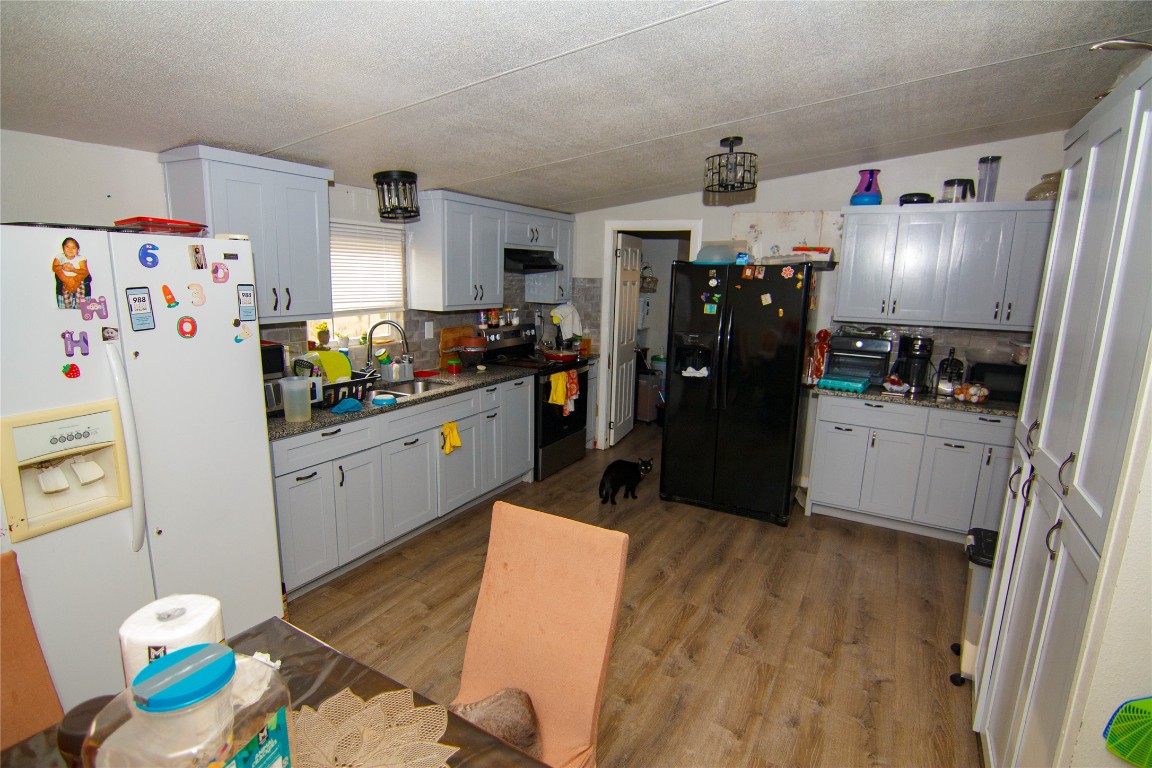 155 Arbuckle Road Elgin, TX 78621 - Photo 10 of 16 Kitchen with vaulted ceiling, white fridge with ice dispenser, black refrigerator with ice dispenser, tasteful backsplash, and electric stove