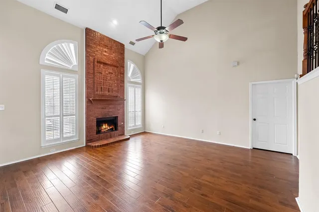 an empty room with wooden floor a chandelier fan a fireplace and windows