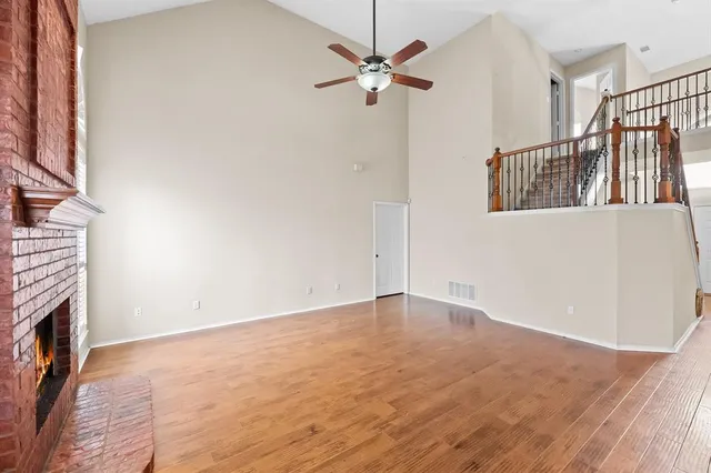 a view of an empty room with chandelier fan and wooden floor