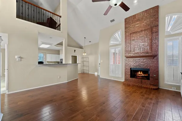 an empty room with wooden floor a chandelier fan a fireplace and windows
