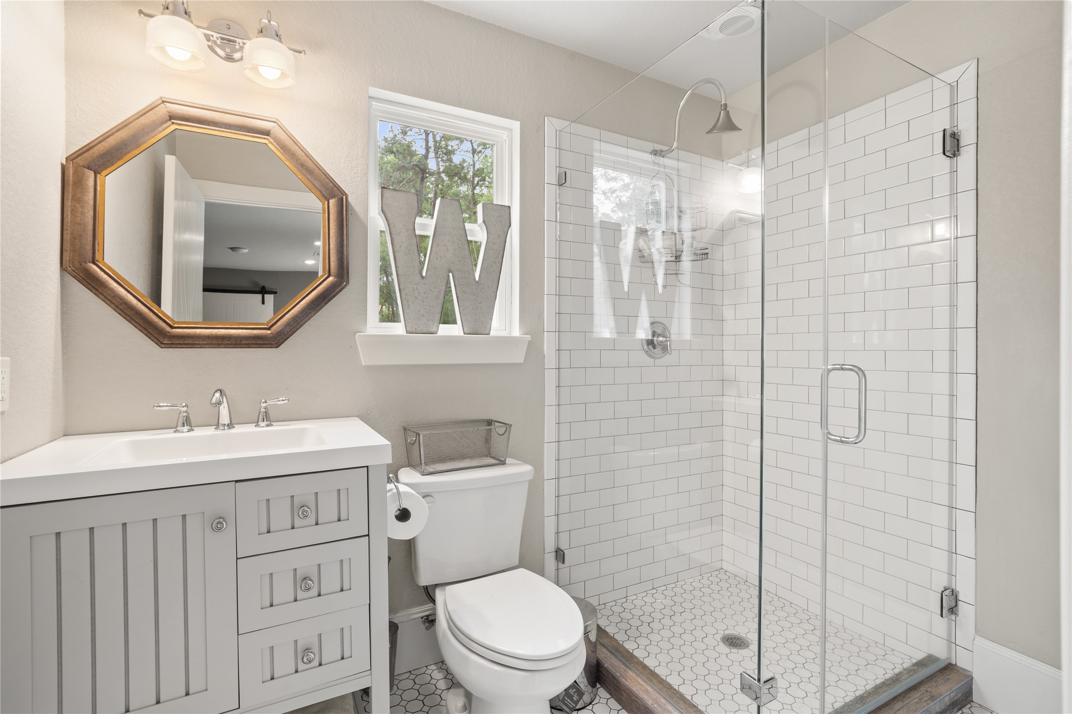 36 Wind River Drive Conroe, TX 77384 - Photo 43 of 45 This bright bathroom features a glass-enclosed shower with white subway tiles, a modern vanity with a stylish octagonal mirror, and a window for natural light.