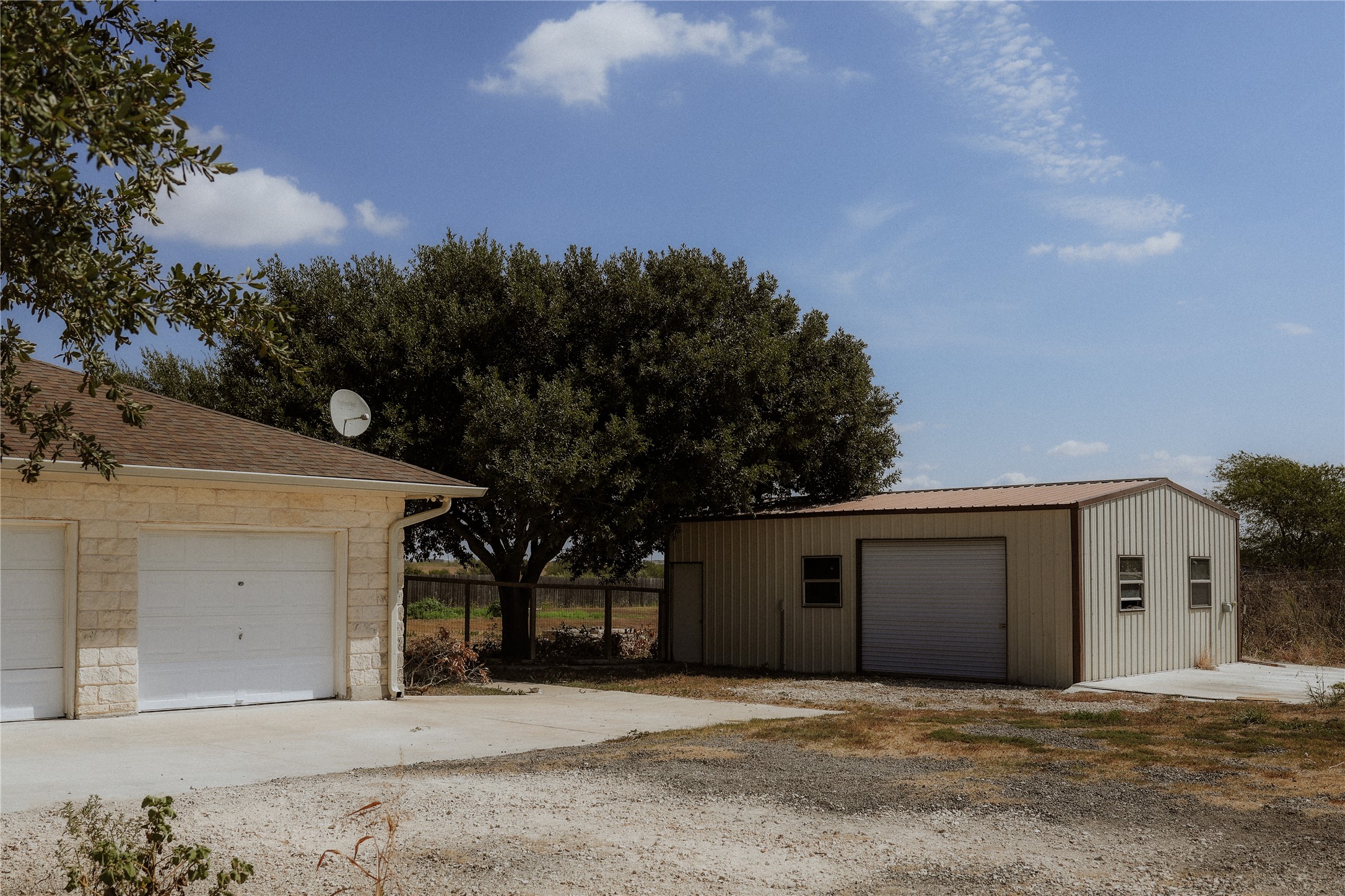17323 Manda Carlson Road Manor, TX 78653 - Photo 27 of 29 A spacious detached metal outbuilding stands alongside a stone-clad garage under a clear blue sky.