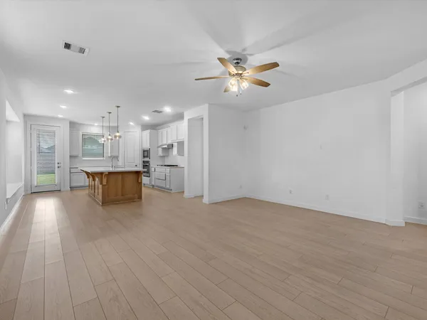 a view of an empty room and kitchen with wooden floor