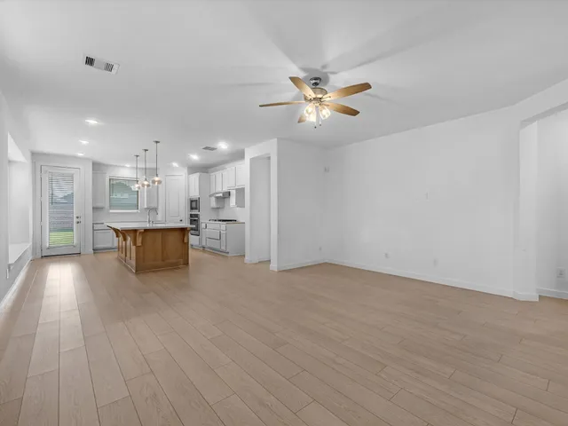 a view of an empty room with wooden floor and a ceiling fan