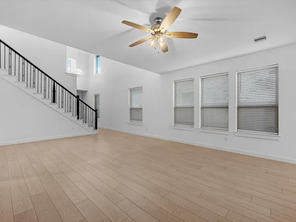 a view of an empty room with wooden floor and a ceiling fan