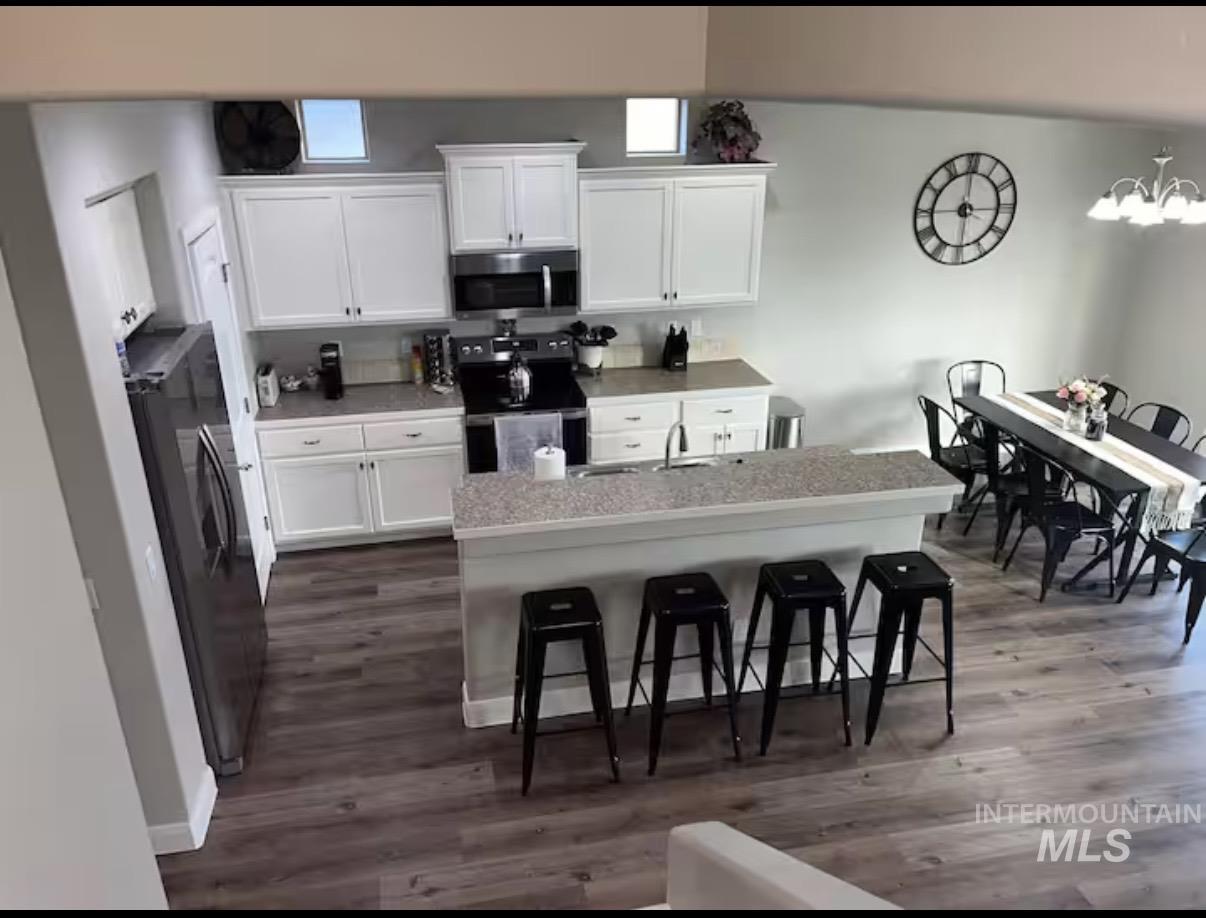 723 Stallion Springs Way Middleton, ID 83644 - Photo 4 of 50 Kitchen featuring white cabinetry, black appliances, a breakfast bar, light countertops, and an island with sink